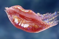 Glossy pink lips with sparkly golden glitter makeup in macro shot against dark blue background, showing glamorous cosmetic application and shine effect.