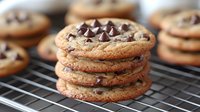 Freshly baked chocolate chip cookies stacked on cooling rack, showing crispy golden edges and gooey chocolate chips, classic homemade dessert treat.