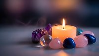 Burning candle surrounded by colorful healing crystals and gemstones creating peaceful meditation atmosphere for spiritual wellness and relaxation practices.