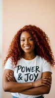 Confident African American woman with curly red hair wearing motivational t-shirt, arms crossed, smiling against neutral background for lifestyle content.