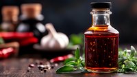 Glass bottle with spicy chili oil, fresh herbs and red hot peppers on dark rustic background. Homemade seasoning for Asian cuisine with aromatic ingredients.