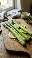 Fresh asparagus spears with lemon slices and sea salt on rustic wooden cutting board in bright kitchen setting for healthy cooking and meal preparation.