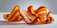 Crispy bacon strips with golden brown edges and marbled fat streaks arranged on clean white background for culinary and breakfast cooking concepts.