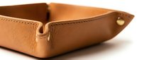 Tan leather valet tray with gold snap detail on white background, showcasing fine stitching and premium texture for luxury lifestyle concepts.