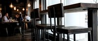 Modern black wooden chairs at dining table in contemporary restaurant interior with blurred guests and warm pendant lighting in background, suitable for hospitality, dining, and interior design projects.