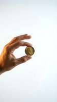 Male hand holding vintage bronze coin between fingers against white background for financial and investment concepts.