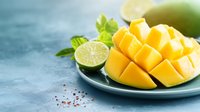 Fresh ripe mango cut in cubes served on blue plate with lime slices and mint leaves on concrete background, selective focus with copy space.