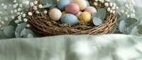 Colorful speckled eggs nestled in rustic wicker basket with delicate white flowers and eucalyptus leaves for Easter spring celebration decor.