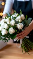 Elegant white rose wedding bouquet with fresh eucalyptus greenery held by bride wearing black, tied with silk ribbon. Close-up view highlights delicate floral details.