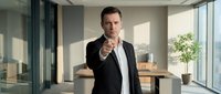 Confident businessman in suit pointing finger at camera in modern office with natural lighting and glass walls for corporate presentations.