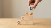 Hand placing wooden block with growth chart icon completing GROW word concept for business development and personal improvement strategies.