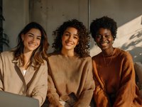 Diverse group of young women in warm-toned sweaters smiling together in soft natural light, creating a cozy and friendly atmosphere for lifestyle and friendship concepts.