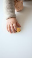 Child hand reaching for golden coin near piggy bank on white background representing early financial education and saving habits development.