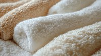 Soft plush microfiber texture close up showing fluffy white and beige towel fabric folds with gentle shadows creating cozy, luxurious feeling for spa and wellness designs.