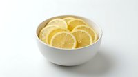 Fresh lemon slices arranged in a white ceramic bowl, isolated on white background. Bright yellow citrus fruit for food and beverage design use.