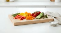 Fresh colorful vegetables sliced on wooden cutting board with herbs and salt bowl in modern kitchen setting for healthy cooking preparation.
