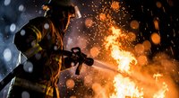 Industrial welder in protective gear working with bright sparks and flames in heavy manufacturing environment. Safety equipment and metalworking process.