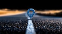 Glowing blue location pin marker floating over asphalt road with white line at dusk, concept of GPS navigation and travel destination point.