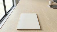 Blank white square tile or ceramic sample on wooden table surface in modern office interior with natural window lighting for design mockup presentations.