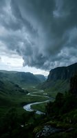 Dramatic storm clouds gather over a winding river cutting through a lush green valley surrounded by steep mountain cliffs and verdant hillsides, capturing moody weather and landscape scenery.