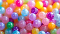 Colorful translucent round beads in pastel and bright colors creating playful pattern. Shiny plastic or glass spheres with soft focus background for jewelry making and crafts.