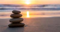 Zen stone stack on beach at sunset with golden light reflection on wet sand creating peaceful meditation atmosphere for wellness and mindfulness concepts.