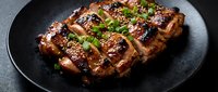 Grilled pork ribs with teriyaki glaze and sesame seeds on dark plate. Barbecue meat with green onions garnish for restaurant menu and cooking content.
