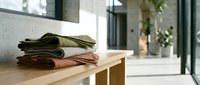 Folded linen fabrics in neutral earth tones stacked on wooden table in bright modern interior space with natural light and minimalist decor.