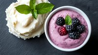 Fresh blackberry and raspberry yogurt mousse with vanilla ice cream scoop and mint leaves on dark slate background, healthy dessert serving.