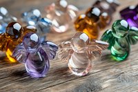 Colorful glass angel figurines arranged on rustic wooden surface, featuring purple, amber, green and clear crystal decorative ornaments with delicate wing details.