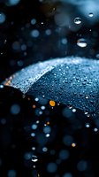 Raindrops on black umbrella at night with bokeh lights creating magical atmosphere. Water droplets glisten against dark background with orange street lights.