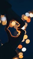 Two hands forming a heart shape silhouette against glowing bokeh lights at night, symbolizing love, romance, and togetherness.