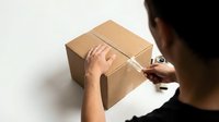 Delivery worker sealing cardboard box with tape, overhead view of packaging and shipping process for logistics and e-commerce operations.