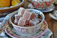 Homemade rose Turkish delight cubes dusted with powdered sugar served in vintage porcelain teacup with floral pattern on rustic wooden table. Traditional Middle Eastern confection.