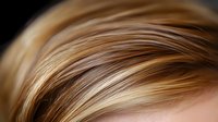 Close up view of blonde highlighted hair with soft focus showing natural wavy texture and dimensional color tones in warm golden and caramel shades.