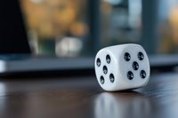 White gaming dice with black dots on wooden table surface, shallow depth of field creates soft blurred background effect, macro photography shows detailed texture.