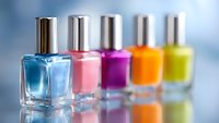 Colorful nail polish bottles in row on reflective surface with blue, pink, purple, orange and yellow shades against soft blurred background. Professional manicure concept.