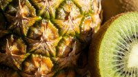Close-up of fresh pineapple texture and sliced kiwi fruit in bright natural sunlight, showcasing vibrant tropical colors and organic details.