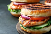 Grilled chicken breast sandwich with fresh vegetables on toasted bun served on wooden board, healthy fast food meal concept for restaurant menu design.