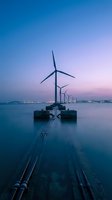 Offshore wind turbines at twilight with purple sky reflection on calm water creating sustainable energy seascape for renewable power generation concepts.