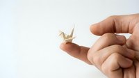Young adult hand holding delicate origami paper crane on white background, isolated for design use on merchandise, crafts, and creative projects.