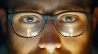 Close up portrait of young caucasian male wearing glasses illuminated by blue computer screen light in dark room, dramatic lighting highlighting eyes and facial features.