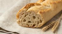 Freshly baked artisan bread loaf sliced on linen cloth with wheat ears, showcasing golden crust and airy texture for bakery and food photography.