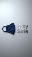 Navy blue fabric face mask beside metallic Stay Safe text on light gray background, promoting health protection and pandemic awareness.