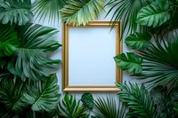 Empty golden frame surrounded by lush tropical leaves including monstera and palm fronds creating natural border against light background. Mockup for artwork.