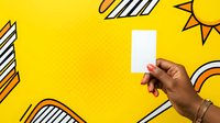 Diverse hand holding blank white card against vibrant yellow pop art background with sun and striped elements, suitable for advertising, marketing campaigns, and promotional material presentations.