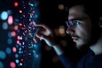 Young male programmer analyzing digital data stream with glowing particles and code visualization in dark tech environment for software development projects.