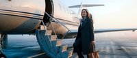Woman in dark coat boarding private jet at sunset, ready for business travel or luxury vacation getaway.