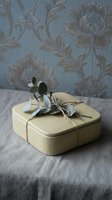 Elegant yellow gift box tied with twine and eucalyptus sprig on linen fabric against vintage floral wallpaper for special occasions and celebrations.