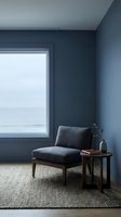 Modern minimalist interior with dark blue upholstered armchair, wooden side table, and large window overlooking seascape. Neutral area rug and calm color palette create serene reading nook.